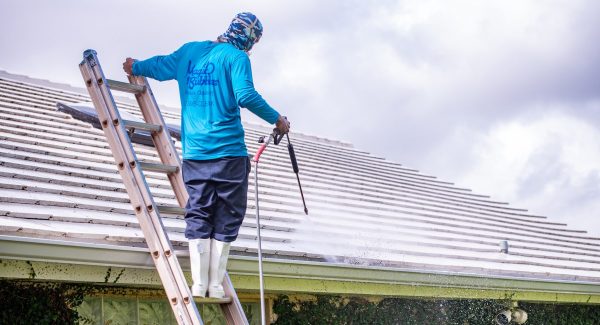 man on ladder pressure washing a roof